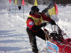 65. Мэнэдэк. Финиширует каюр № 19. На нартах плакат - священник Владислав. Март 2013.jpg